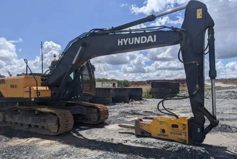Hyundai crawler excavator with a Dozco D135 hydraulic rock breaker attachment at a construction site.