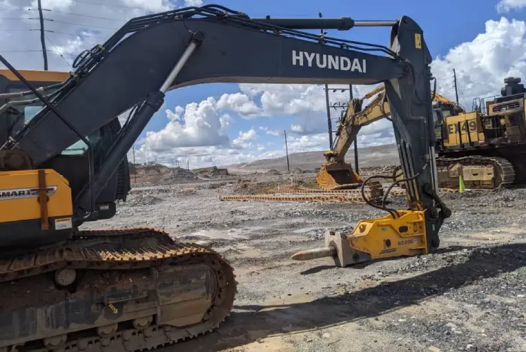Hyundai crawler excavator with a hydraulic breaker attachment on a rocky construction site.
